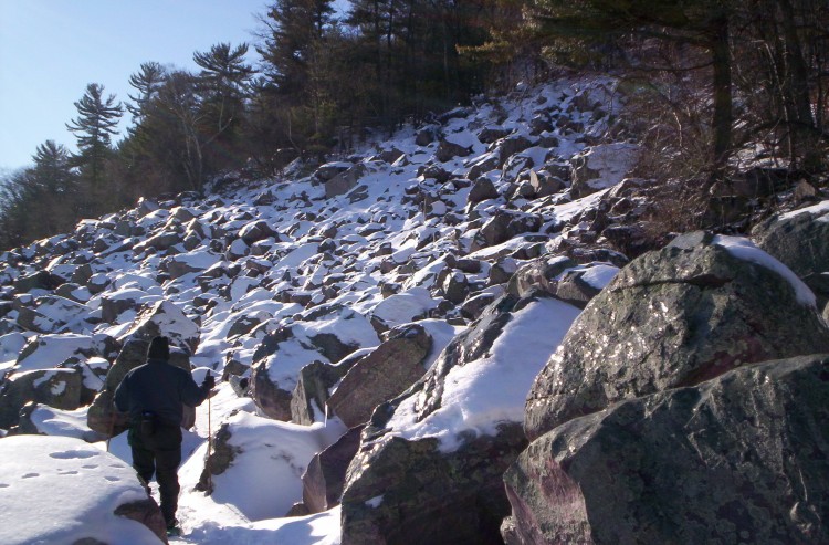 man snowshoeing amid snow covered rock field