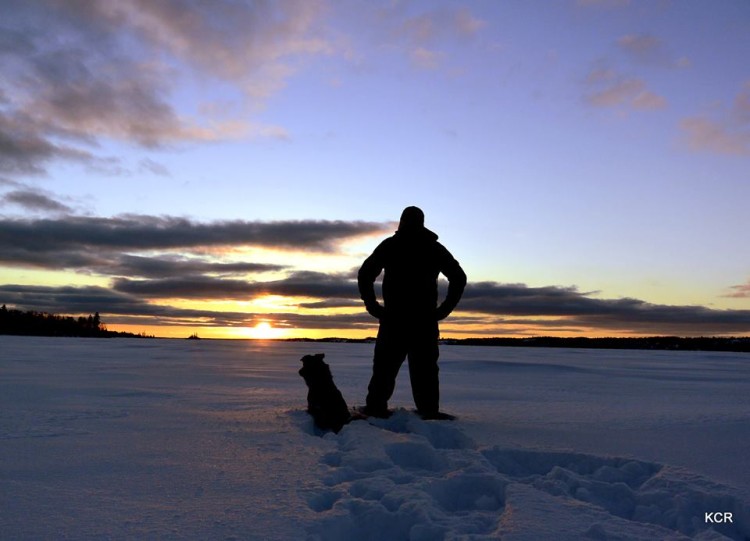 man and dog watching sunset in the snow