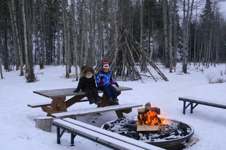 two kids sitting on table in snow by fire