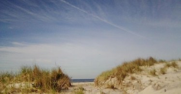 view of sand dunes under open blue sky and wisps of clouds