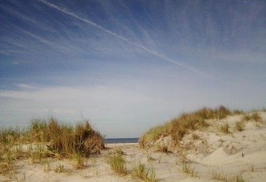 view of sand dunes under open blue sky and wisps of clouds