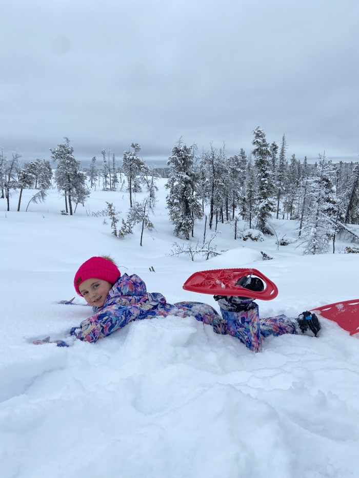 child laying in the snow with snowshoes and trees in background