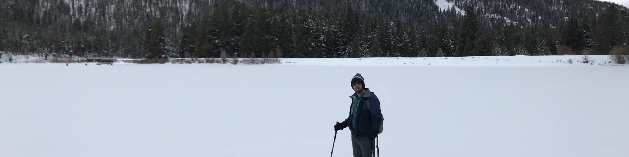 man standing on snowy frozen lake in snowshoes