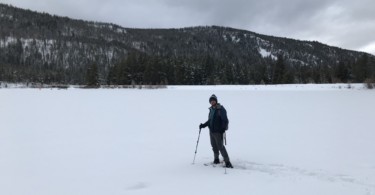 man standing on snowy frozen lake in snowshoes