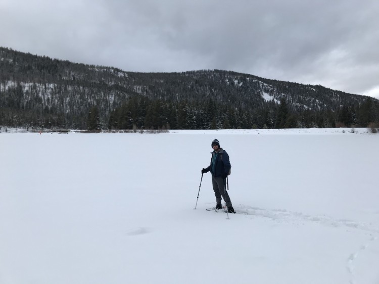 man standing on snowy frozen lake in snowshoes