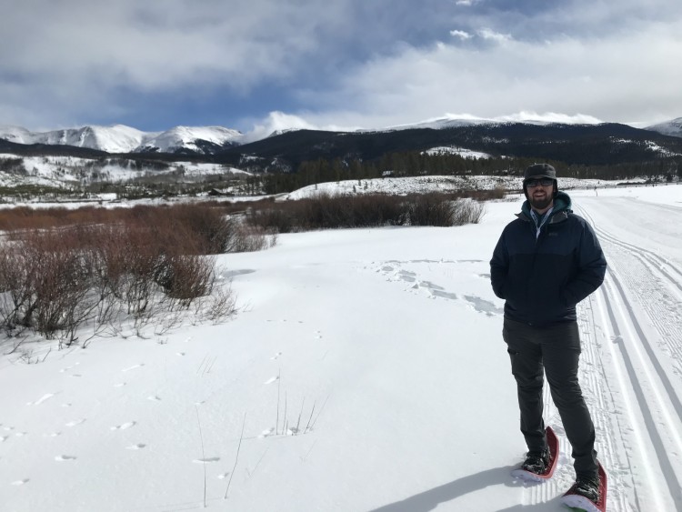 snowshoeing tips for etiquette: man with snowshoes standing on side of trail