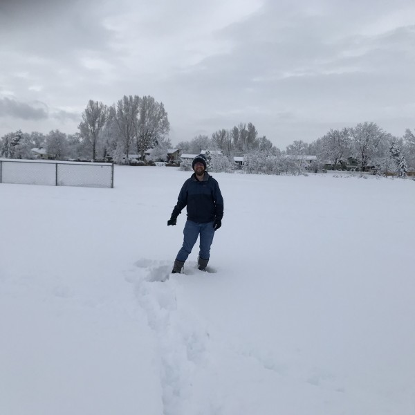 man snowshoeing in park, sinking to mid calf in foot of fresh snow