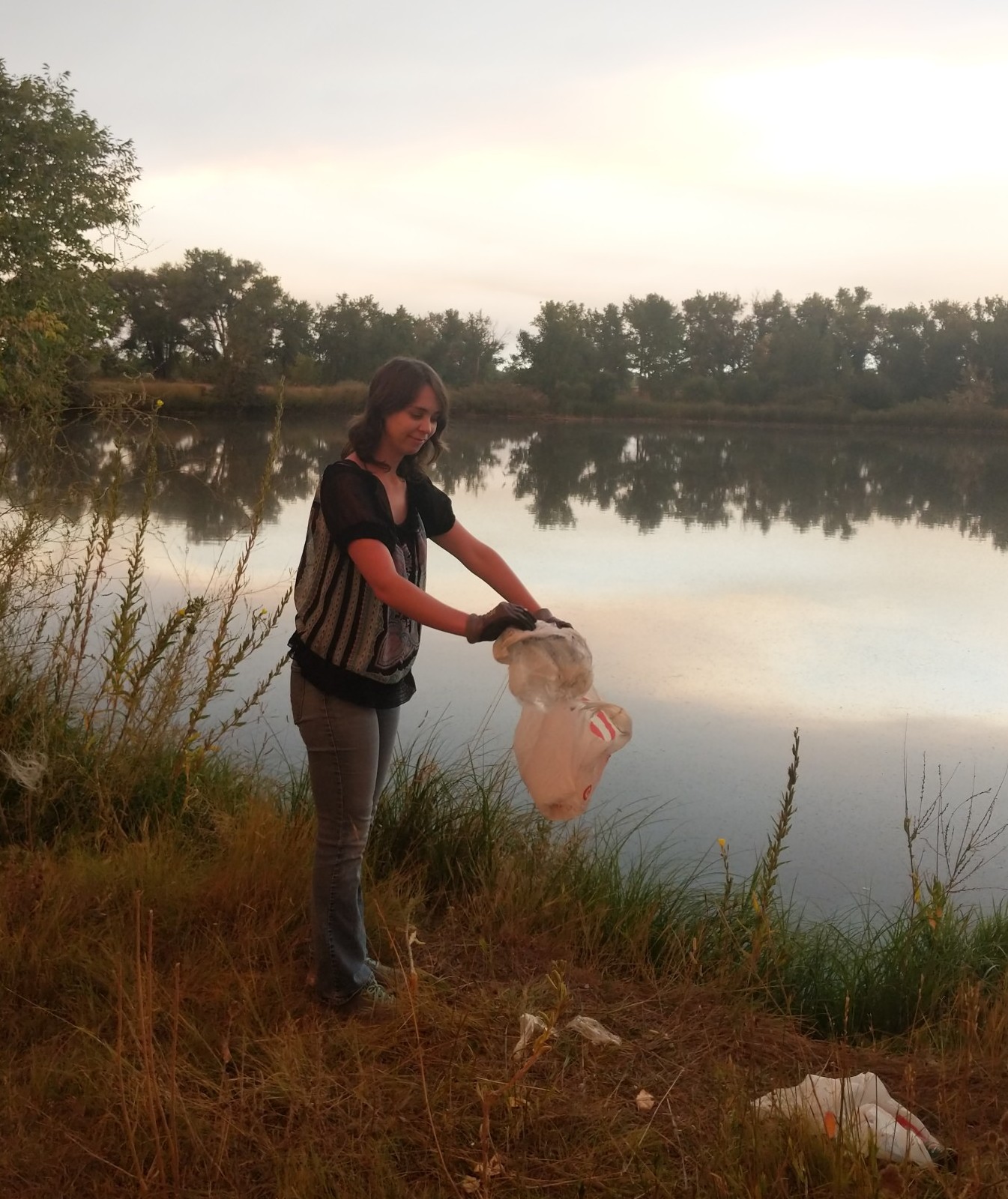 woman picking up trash next to lake