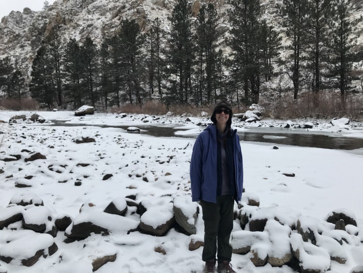 woman standing in snow near river and rocks