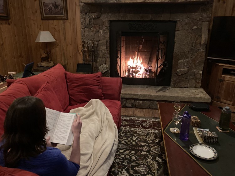 person reading under blanket on the couch by the fire in cabin in Colorado wilderness