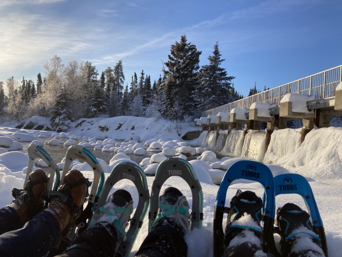 snowshoes lined up in front of river with blue sky above