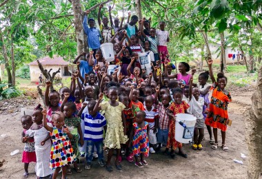 group of children in Liberia with hands in the air and holding Sawyer filters