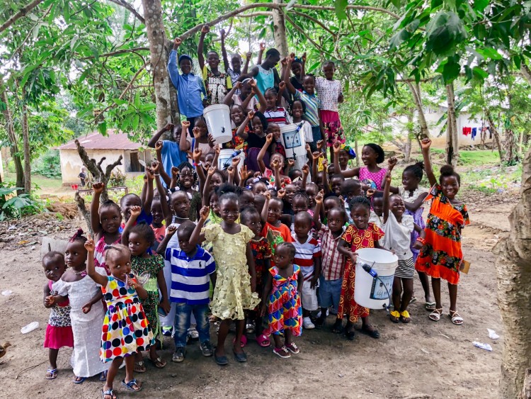 group of children in Liberia with hands in the air and holding Sawyer filters