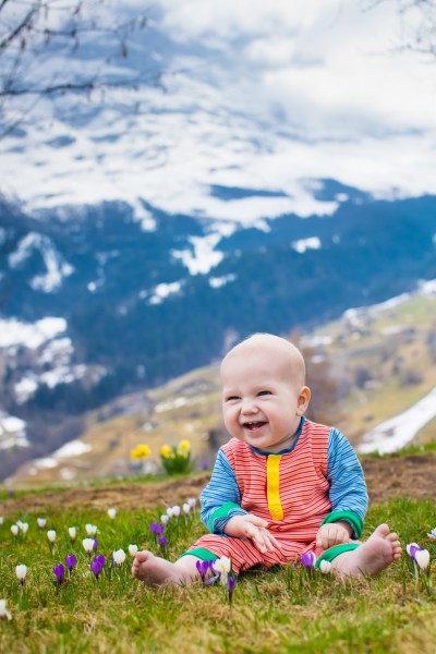 baby smiling and sitting in flowered meadow with snowy mountains in background