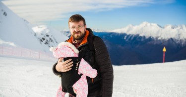 man with baby in front backpack carrier in mountains with snow