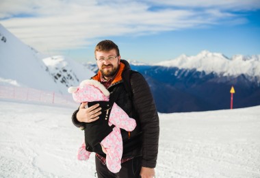 man with baby in front backpack carrier in mountains with snow
