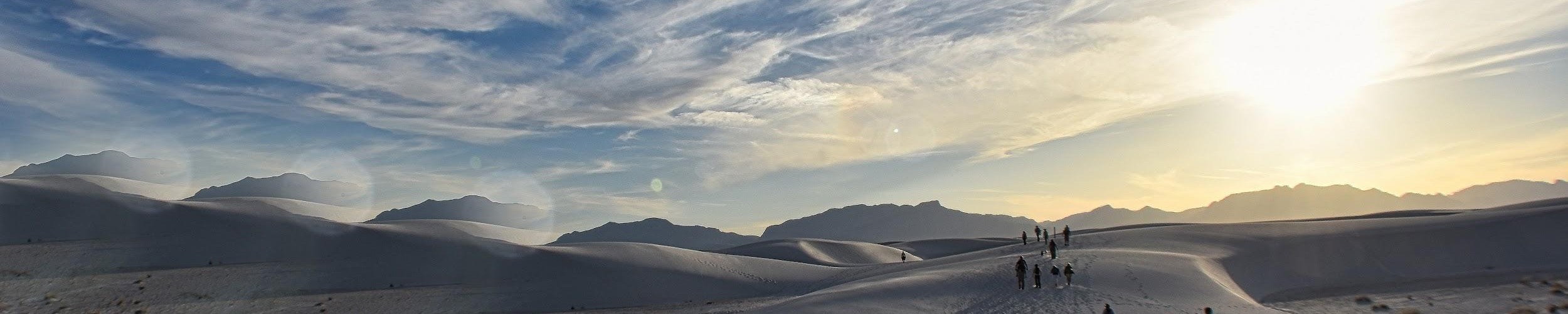 dunes with hikers in distance under clouds and sun