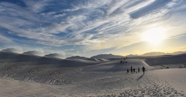 dunes with hikers in distance under clouds and sun