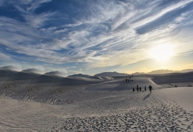 dunes with hikers in distance under clouds and sun
