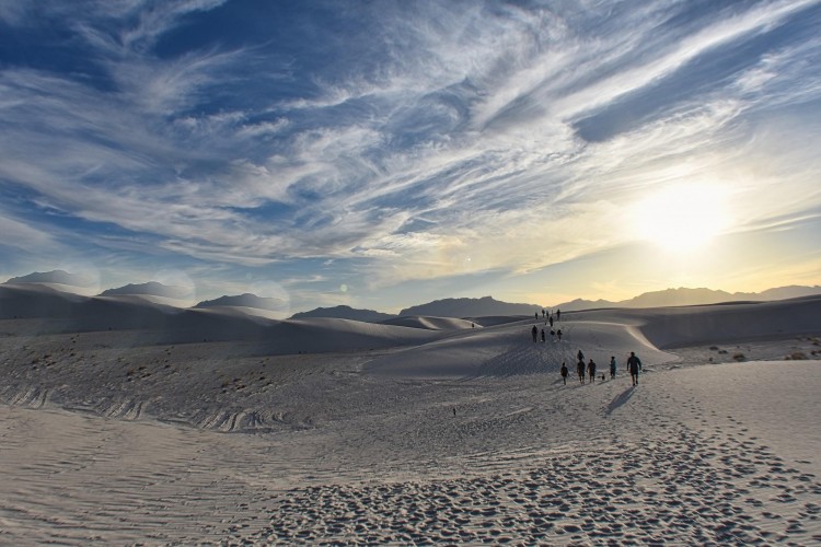 dunes with hikers in distance under clouds and sun