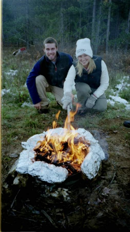 man and woman prepping food over campfire in winter