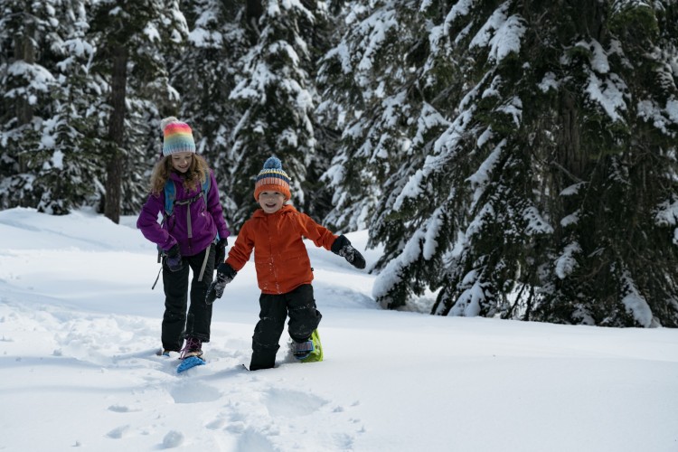 kids on snow with trees in background wearing Crescent Moon snowshoes