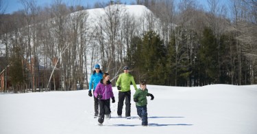 family snowshoeing with trees and a hill in the background