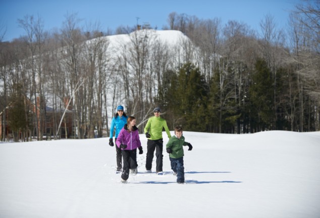 family snowshoeing with trees and a hill in the background