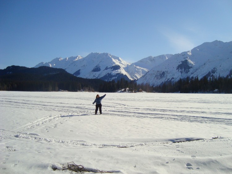 woman far away on snow with arms raised and mountains in background
