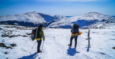 two hikers on top of snowy mountain looking at the view during winter