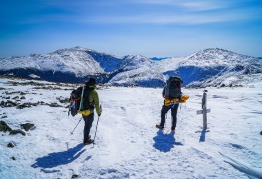 two hikers on top of snowy mountain looking at the view during winter