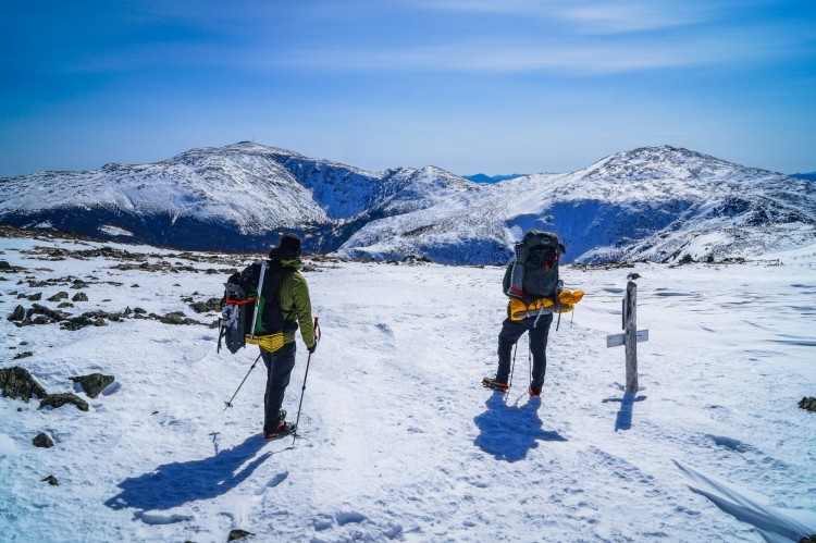 two hikers on top of snowy mountain looking at the view during winter