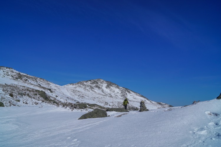 two people snowshoeing in background with mountain peak and blue sky overhead