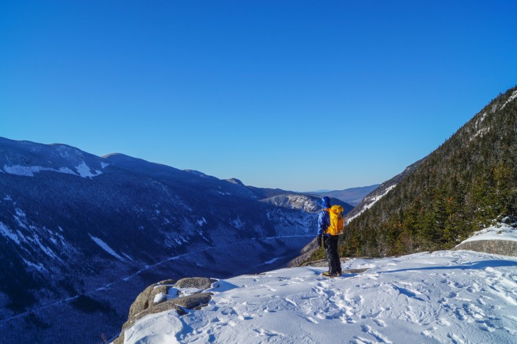 person in distance staring at view on snow in puffy coat and backpack