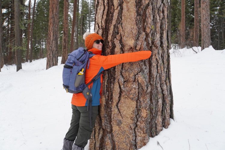 woman with her arms around a tree and smiling