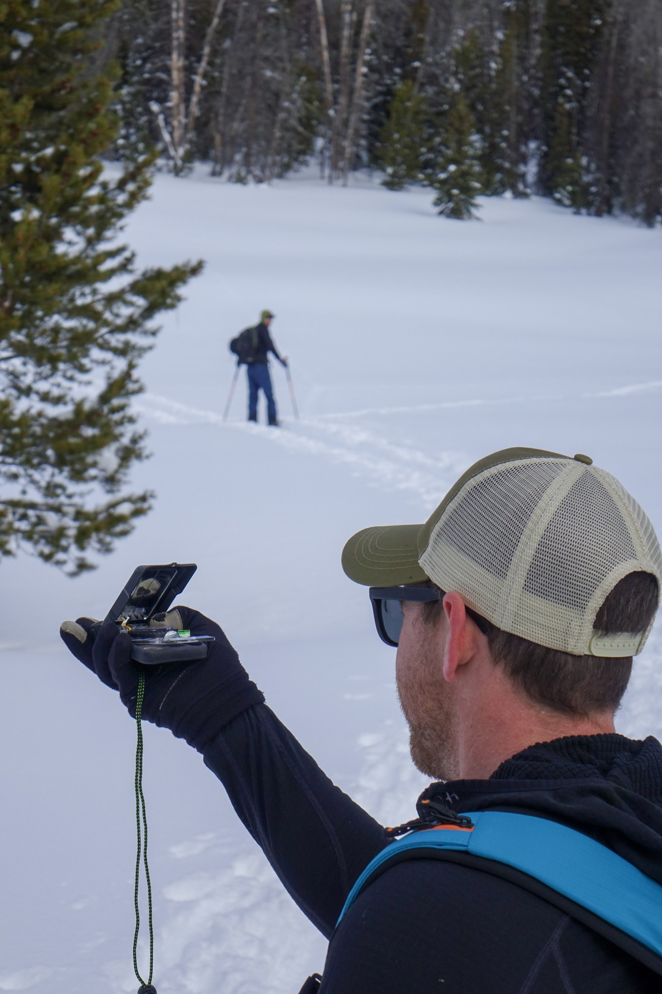 person taking a bearing on snowy trail with another snowshoer up ahead of them