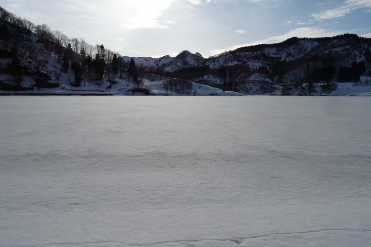 snow covered lake with mountains and open sky in background