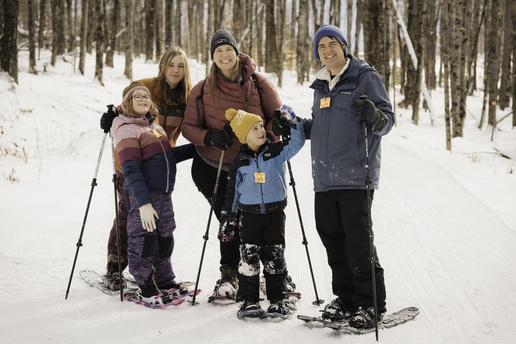 family with snowshoes posing near trees
