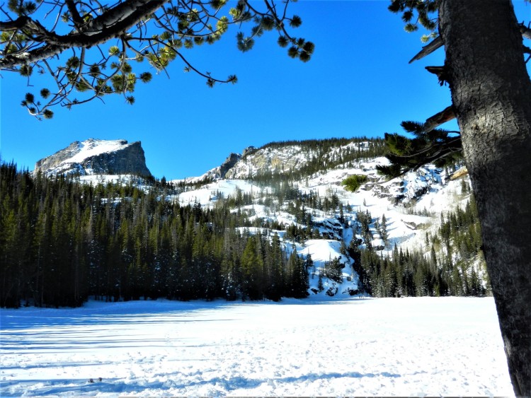 lake covered in snow with mountains in background and blue sky