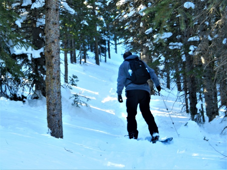 tips for rmnp winter: man snowshoeing on a snowy hill with backpack