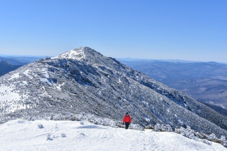 person in red puffy coach walking in distance on mountain top with snow