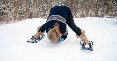 yoga in the snow: woman doing a wide forward fold on snowshoes