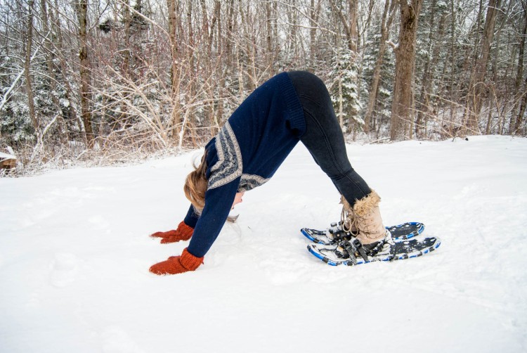 Woman on snowshoes in downward facing dog position surrounded by snow
