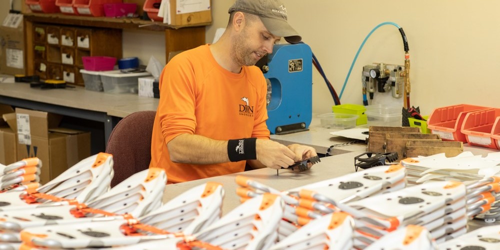 person next to many pairs of snowshoes in factory