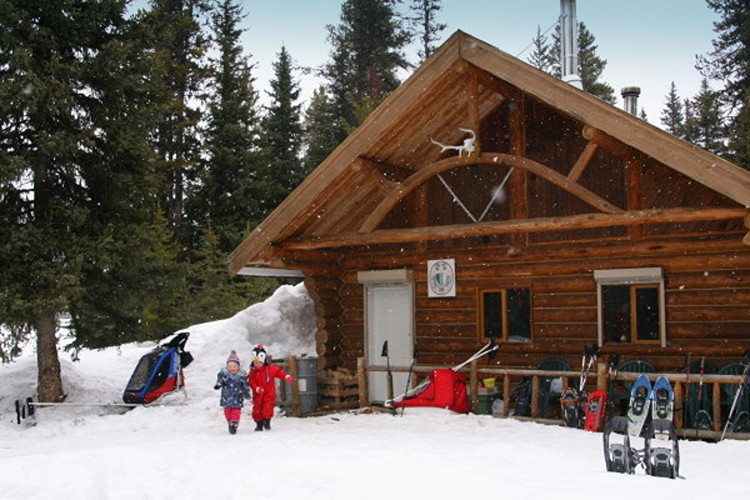 cabin with snow in foreground and two children