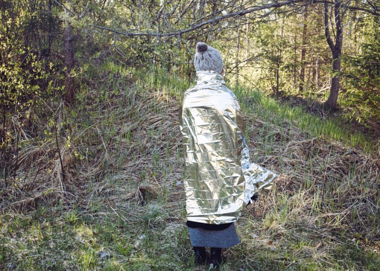 woman with back turned using emergency blanket in forest