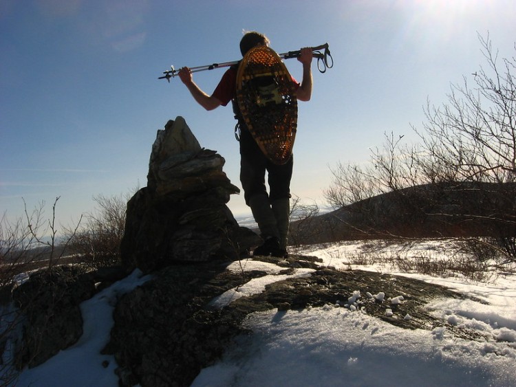 man carrying poles with snowshoes strapped to pack under blue sky