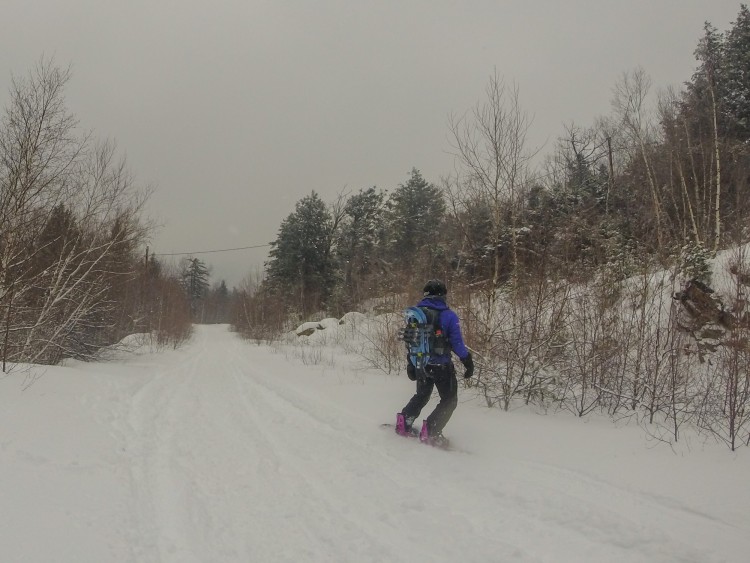 person snowboarding with snowshoes attached to the front of their pack