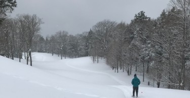 man snowshoeing on golf course with hills under gray sky