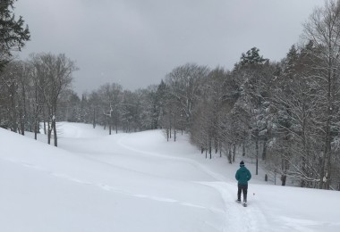 man snowshoeing on golf course with hills under gray sky
